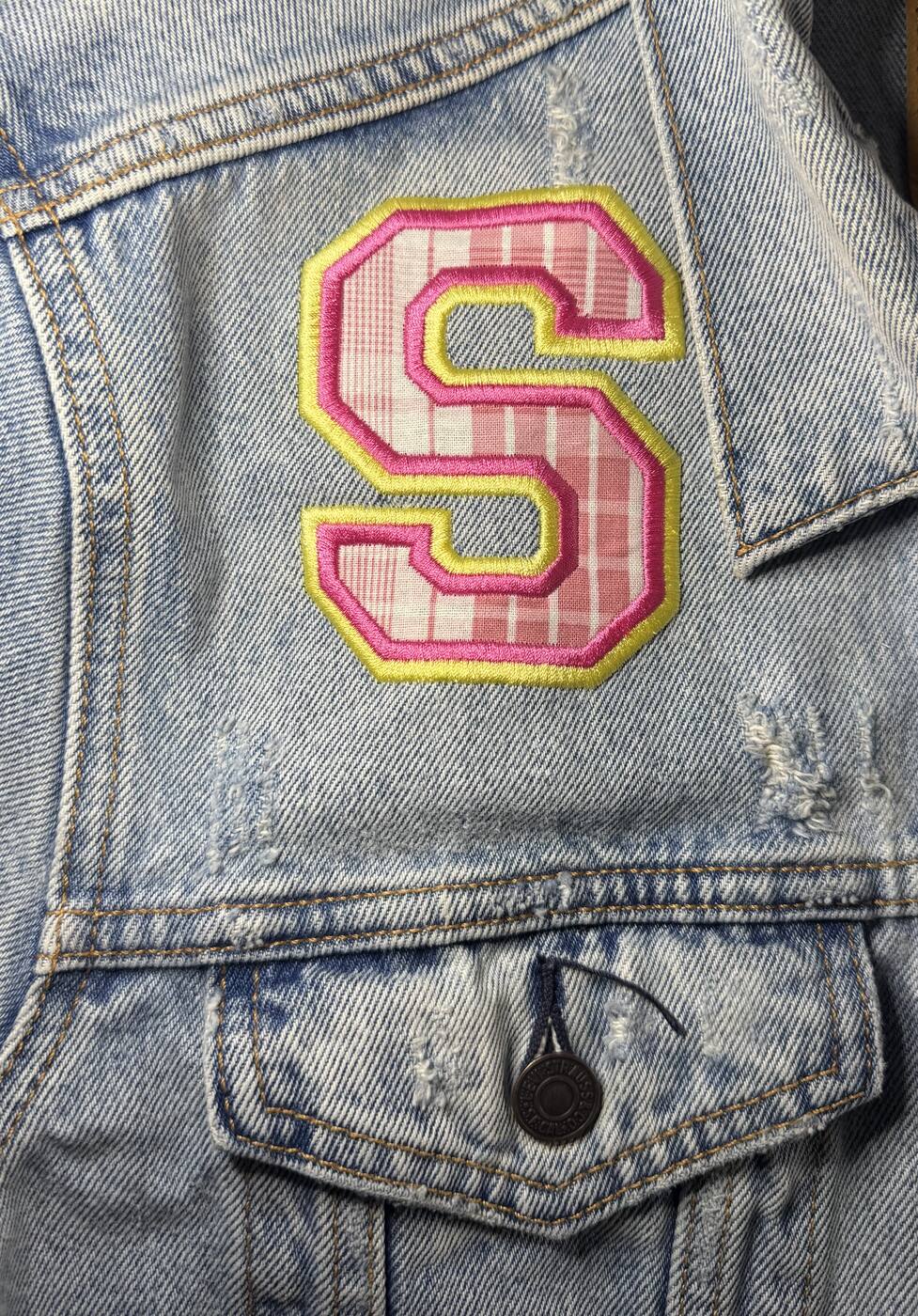 Pink and yellow varsity S patch on a denim jacket